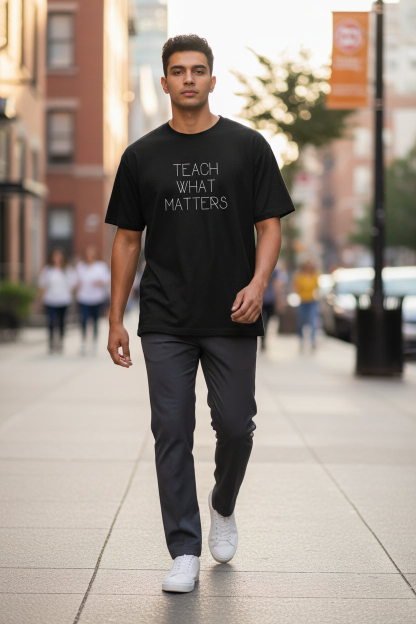 Man wearing a black t-shirt with 'TEACH WHAT MATTERS' text on a city street.